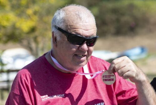 Randy's Project Worker Geordie smiling holding up a medal after completing a sponsored walk for YMCA DownsLink Group