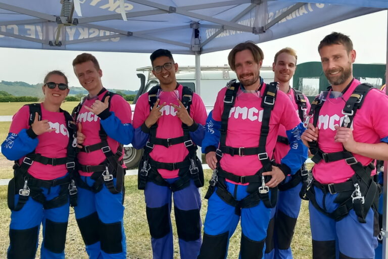 skydive group standing in a line smiling, ready to start. All 6 people are wearing pink YMCA tshirts
