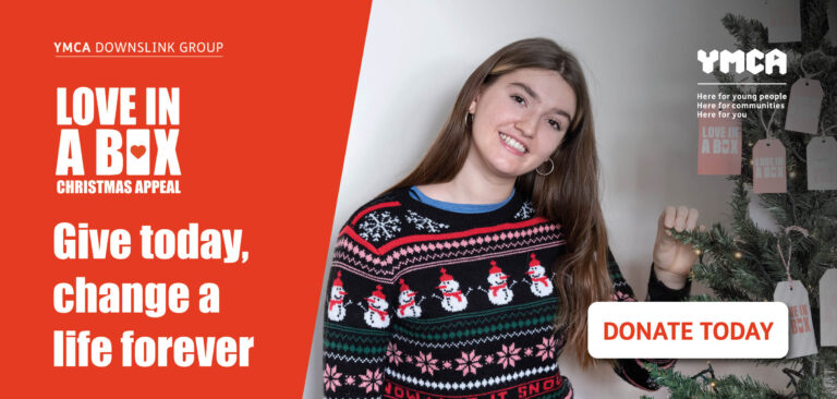 Christmas Appeal love in a box. Young woman smiling wearing a Christmas patterned jumper touching a Christmas tree. 