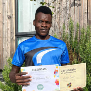 Nader, one of the young people living in our supported housing. He is smiling holding up two certificates