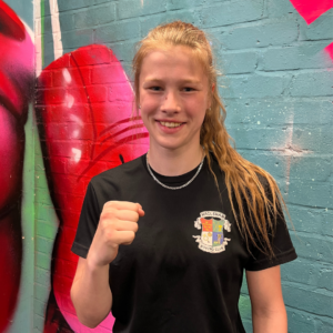 Dee, a young person in our care. She is smiling holding up a fist in her boxing gym