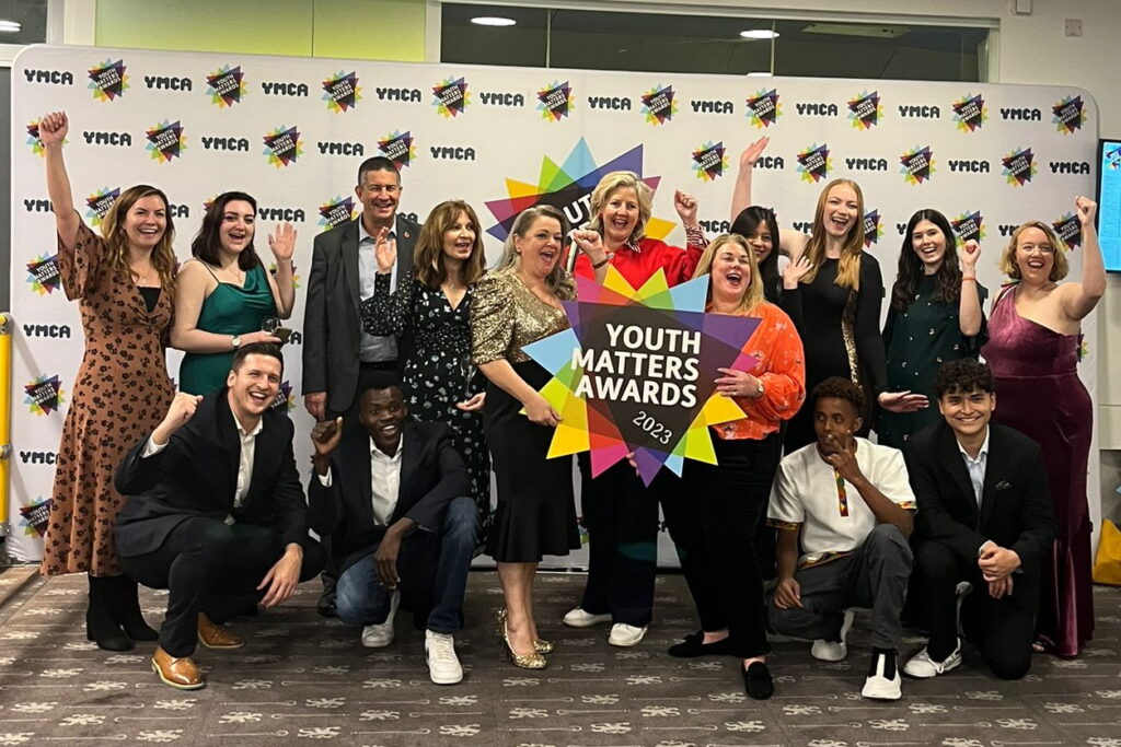 Youth Matters Awards 2023, the whole of the YMCA DownsLink Group team smiling with their fists in the air holding a colourful 'Youth Matters' sign