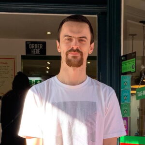 Ex resident, young person, Ben standing smiling at the camera outside a cafe