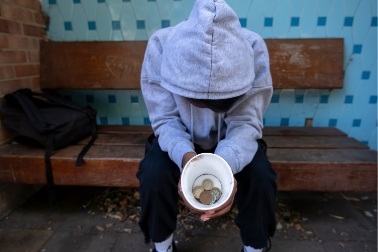 Young person facing homelessness sat on a bench asking for money