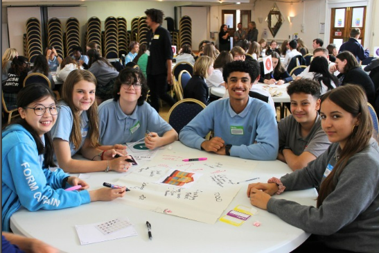 A group of young people in blue school uniform sat on a table at the Mental Health Champions celebration event.