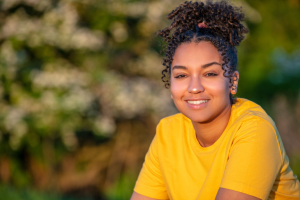 Image of young woman smiling with brown hair, wearing a yellow tshirt.