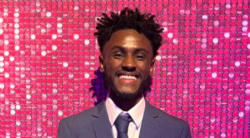 Adi smiling at the Youth Matters Awards with a pink glitter background