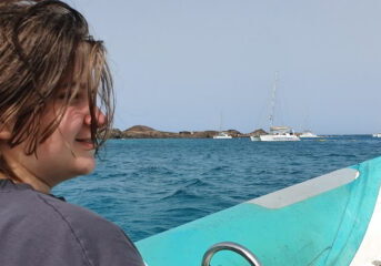 Sam sat on a boat with the sea behind him and a white boat in the distance