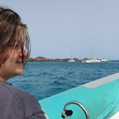 Sam sat on a boat with the sea behind him and a white boat in the distance