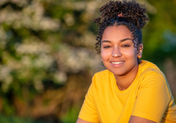 Image of young woman smiling with brown hair, wearing a yellow tshirt.