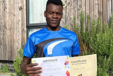 Nader stood in the garden in a blue sports tshirt holding up two certificates of achievement