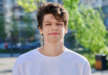 A young man Liam, stood outside wearing a white t-shirt