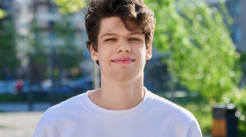 A young man Liam, stood outside wearing a white t-shirt